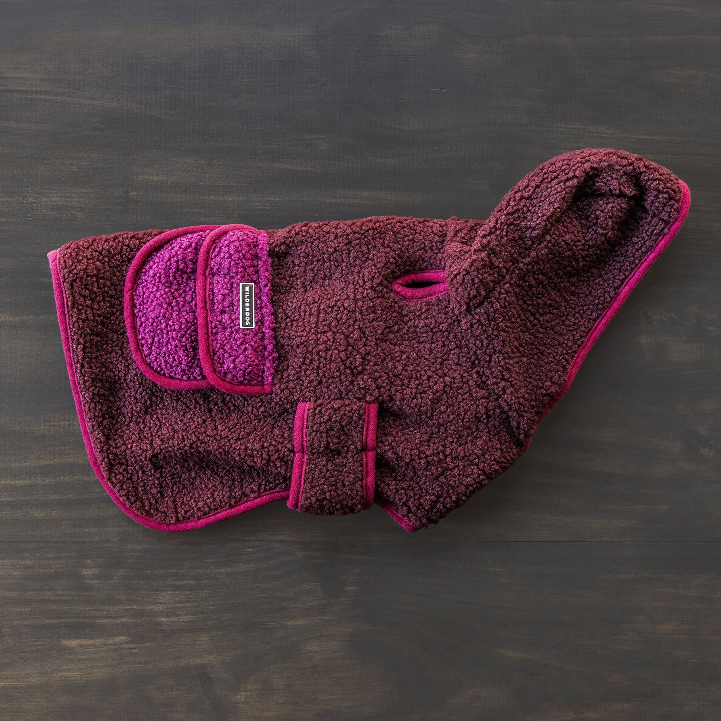 A Sherpa Jacket in pink and purple, crafted from soft, textured fleece fabric, is displayed against a dark background. This dog coat includes a pocket, an adjustable strap, and a handy leash hole for extra warmth and comfort.