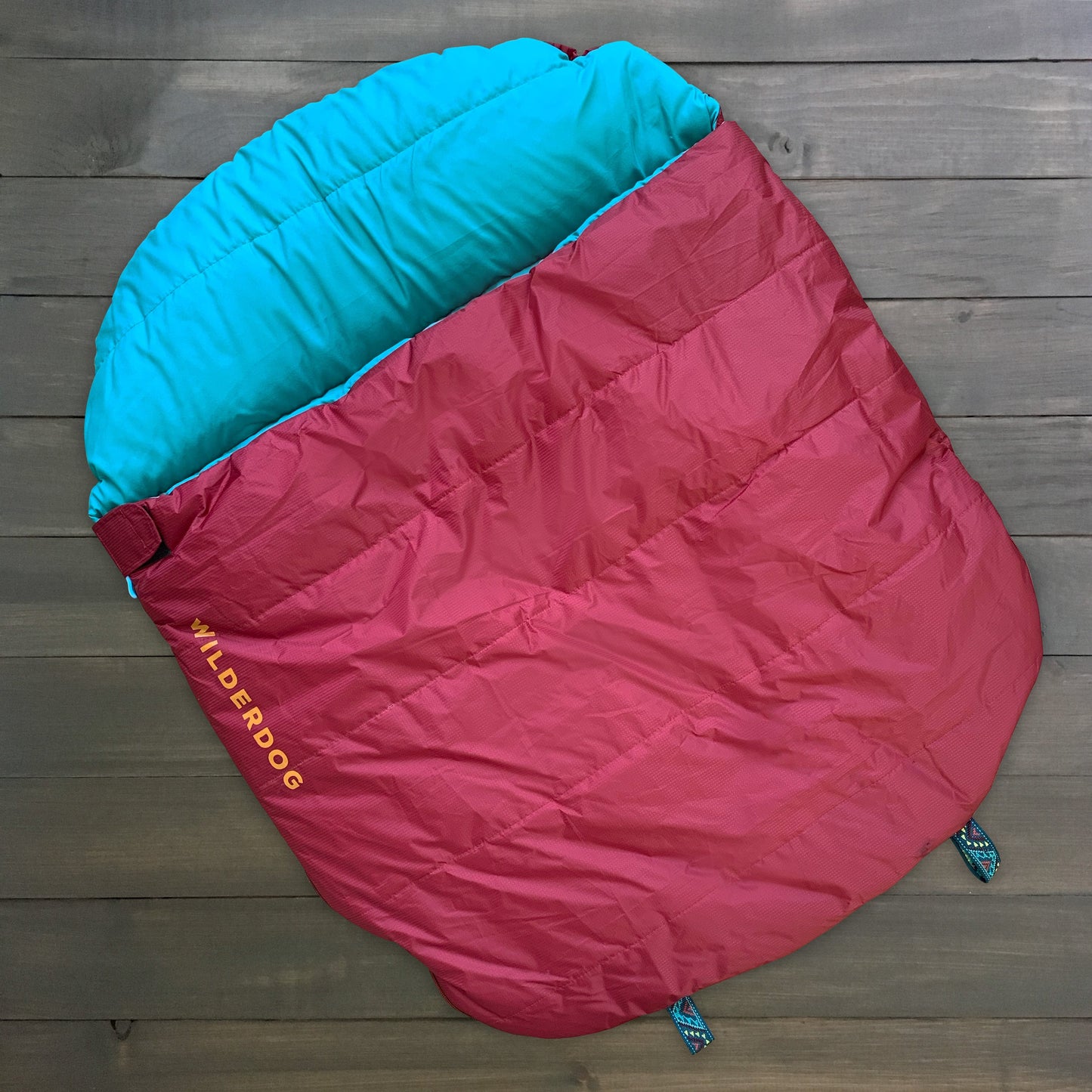 Red and blue "Sleeping Bag" with "WILDERDOG" branding in yellow, laid on a wooden floor.