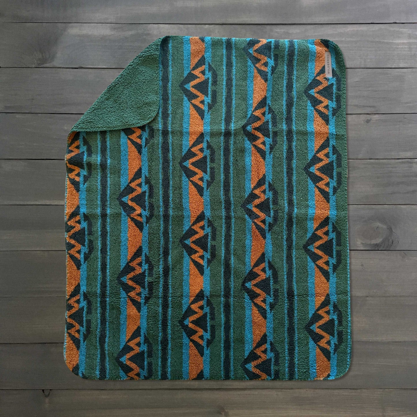 Waterproof Sherpa fleece blanket with blue, orange and green geometric pattern on a dark wood floor