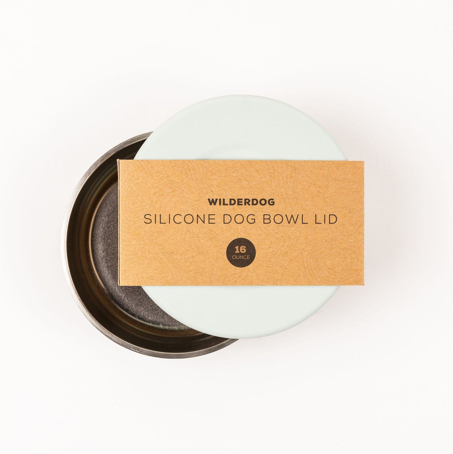 A round, light blue food-grade silicone bowl lid from Wilderdog is placed slightly off-center on a metallic dog bowl. The lid, which fits 16-ounce bowls, has a brown label that reads "Wilderdog Silicone Dog Bowl Lid." It is dishwasher safe and perfect for stainless steel dog bowls. The background is white.