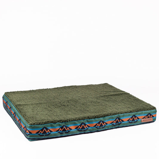 Product Description: The Memory Foam Dog Bed - Replacement Cover features a rectangular design with a green, textured top surface and vibrant sides adorned with zigzag patterns in black, orange, and blue. It includes a side tag that reads "Wilderdog." For added comfort, the cover boasts a Sherpa-fleece top against a plain white background.