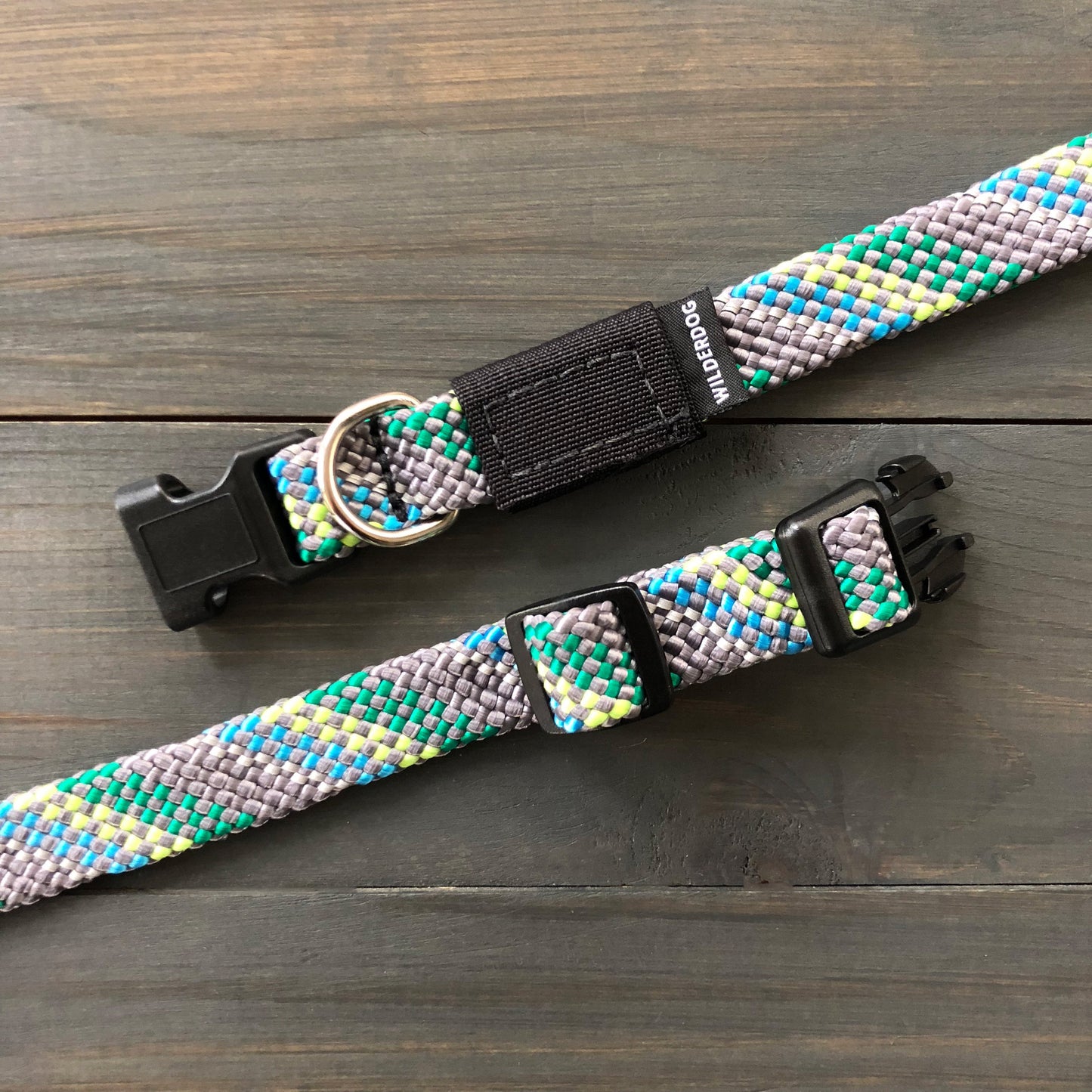 The Alpine Reflective Collar and matching leash set, crafted with the durability of rock climbing rope, displayed on a wooden surface. Featuring a blend of gray, blue, green, and yellow patterns, it includes black plastic clips and a silver D-ring for tags or leash attachment.