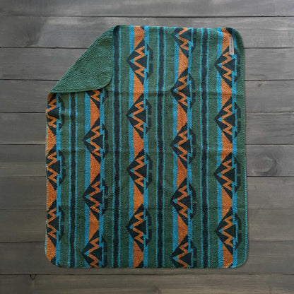 Waterproof Sherpa fleece blanket with blue, orange and green geometric pattern on a dark wood floor