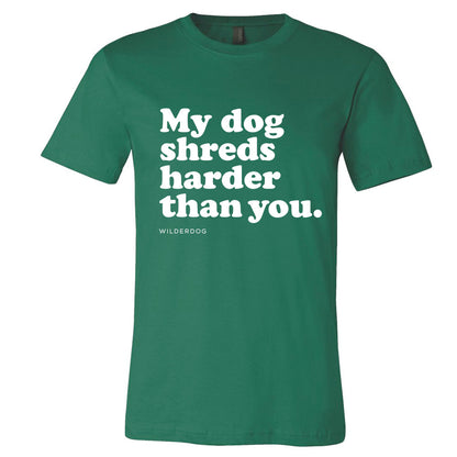 Introducing the Party Dog Tee Shirt: This vibrant green, sustainably produced unisex t-shirt features white text that reads "My dog shreds harder than you," centered on the chest. Below in smaller letters, you'll find the brand name "Wilderdog," making this shirt a fusion of style and eco-friendliness.
